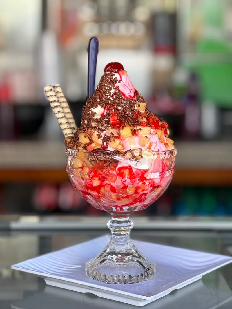 Taça de vidro com sorvete expresso, calda de morango, granulado de chocolate, canudos de wafer e cereja